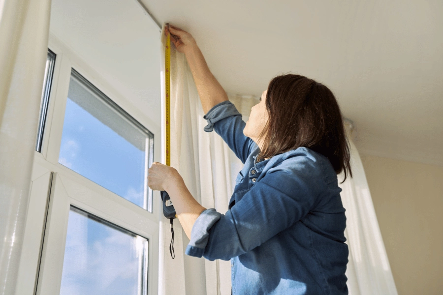 woman measuring a room floor to ceiling with a tape measure
